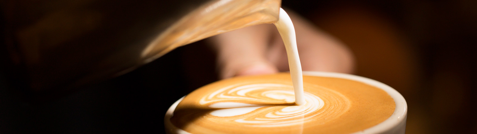 Milk being poured into a latte in a mug.